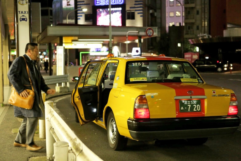 Taxi Nhật Bản đang đón khách tại Kumamoto tại một khu vực đô thị vào buổi tối.