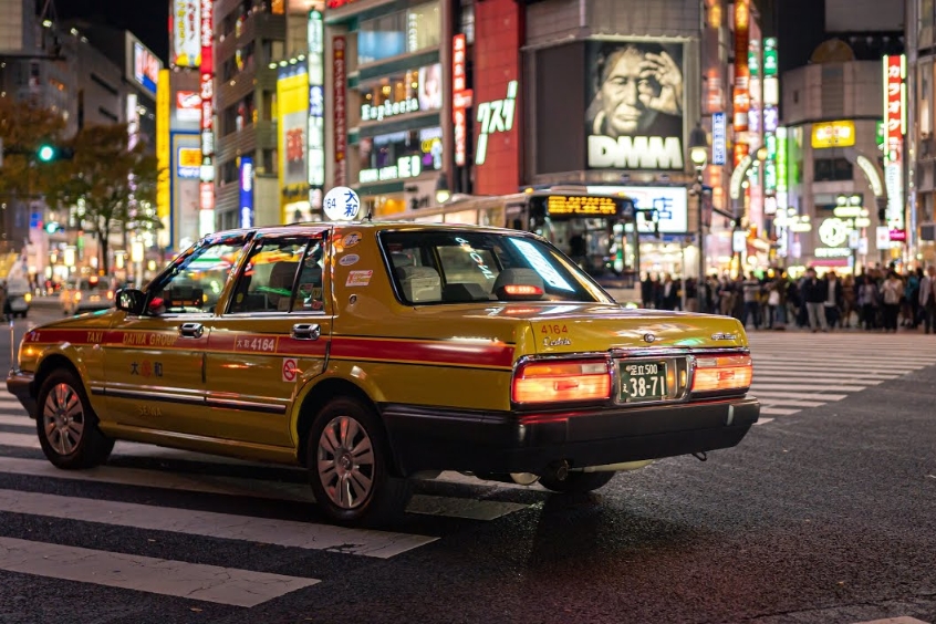 Taxi Nhật Bản di chuyển qua khu vực đô thị sôi động vào ban đêm.