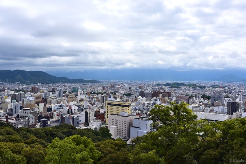 Cảnh thành phố Matsuyama từ trên cao, nhìn thấy sự kết hợp giữa các tòa nhà hiện đại và thiên nhiên xung quanh.