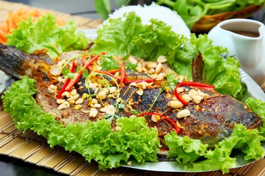 Cá lóc nướng trui da cháy xém giòn rụm, ăn kèm rau sống và nước mắm chua cay đặc trưng miền Tây