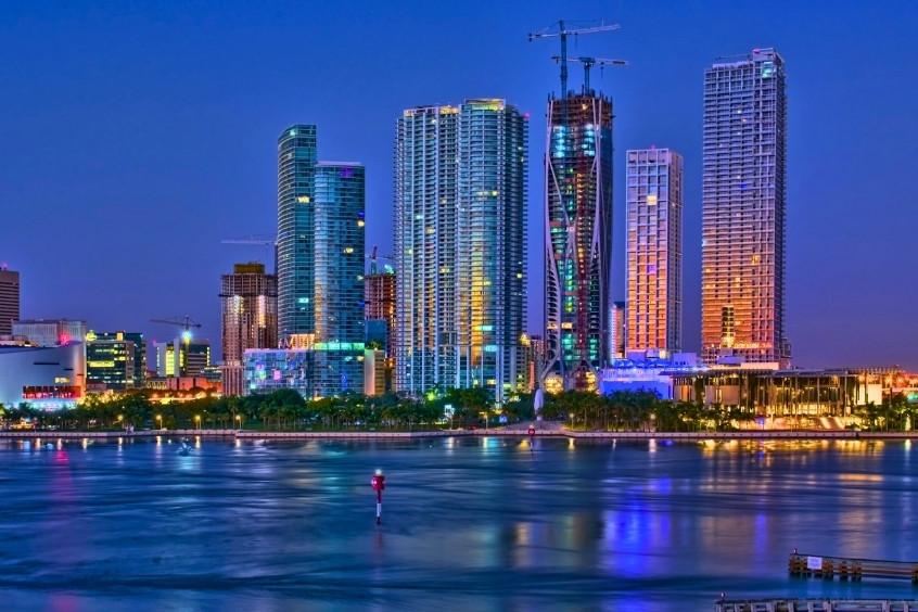 Toàn cảnh trung tâm thành phố Miami về đêm với các tòa nhà chọc trời hiện đại rực sáng ánh đèn, phản chiếu lung linh trên mặt nước vịnh Biscayne