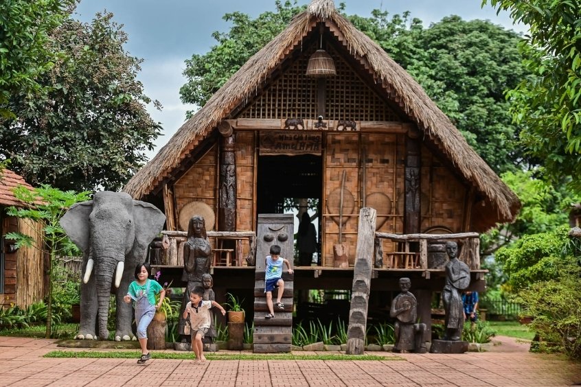 Ngôi nhà dài Ê Đê cùng tượng gỗ và trẻ em vui chơi, lưu ý về văn hóa bản địa và cách ứng xử khi đến Đắk Lắk (Nguồn: Internet)