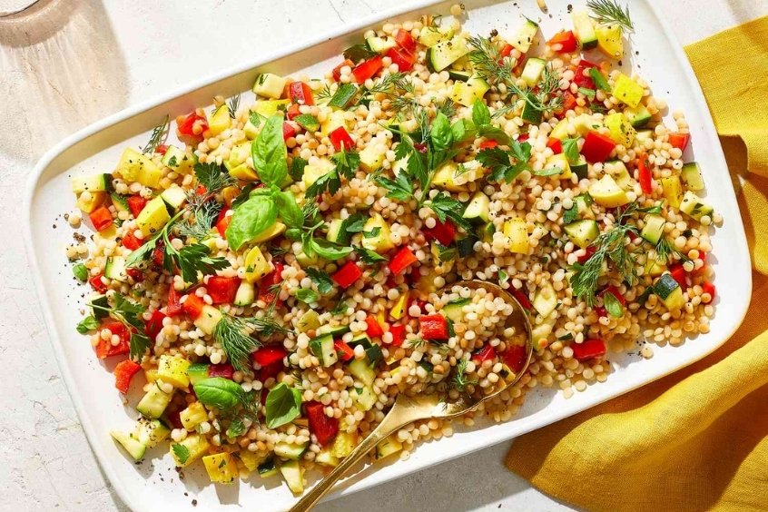 Hạt lúa mì Couscous màu vàng nhạt được bày trên đĩa cùng rau củ và thảo mộc tươi