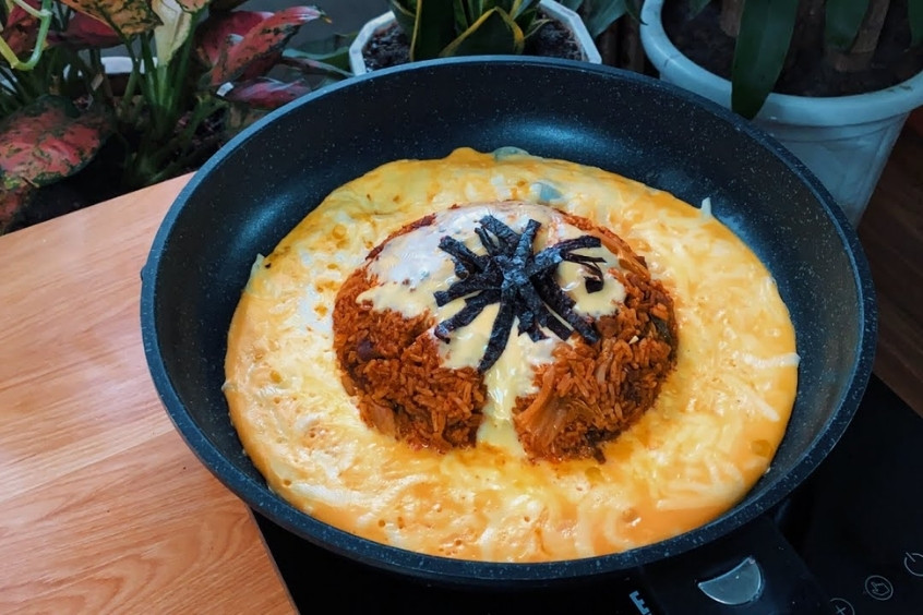 Đĩa cơm chiên núi lửa đang được rưới sốt, với trứng cuộn bồng bềnh như dung nham và khói bốc