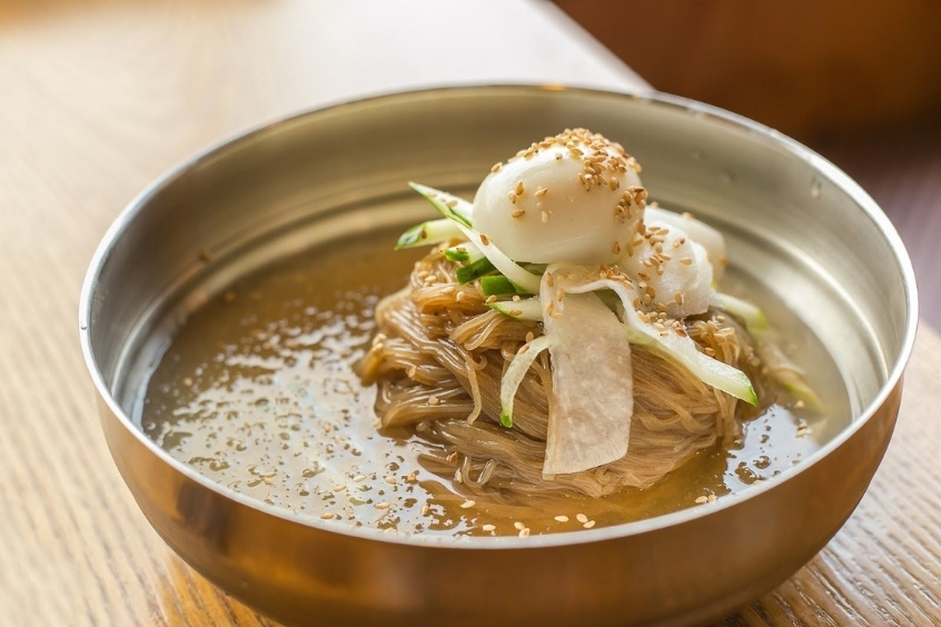 Bát mì lạnh với sợi mì dai, nước dùng trong veo, có đá bào, ăn kèm thịt bò, dưa chuột và trứng luộc